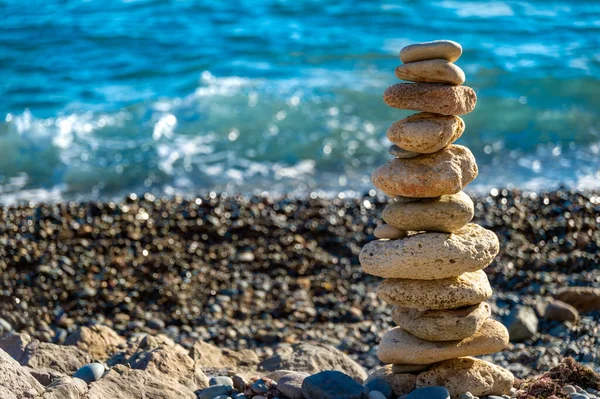 Pyramid on the seashore of stones on a pebble beach against the background of sea waves. The concept of harmony and balance. Peace of mind and spirit.