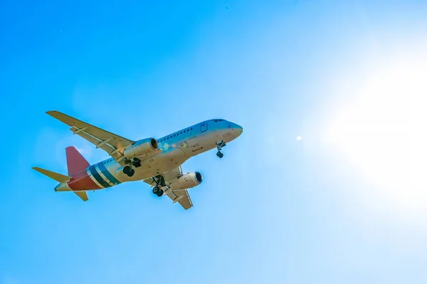 An airplane flies across the sky against the backdrop of the bright summer sun. Beach vacation. Passenger air transportation, air travel. Vacation flights.
