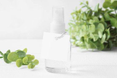 Beyaz kare etiketli yeşil arka planlı el dezenfektanı şişesinde. Temizleyici sprey şişesi. Sprey şişeye etiket as. Düğün hediyesi etiketi, parti hediyesi etiketi, teşekkür etiketi. ön görünüm, beyaz kopyalama alanı. 