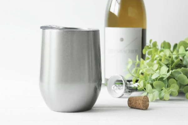 Silver wine tumbler mockup with wine bottle, bottle opener, cork and greeneries at the background. Drink mockup. Wine tumbler with lid. Front view, copy space, svg product mockup.