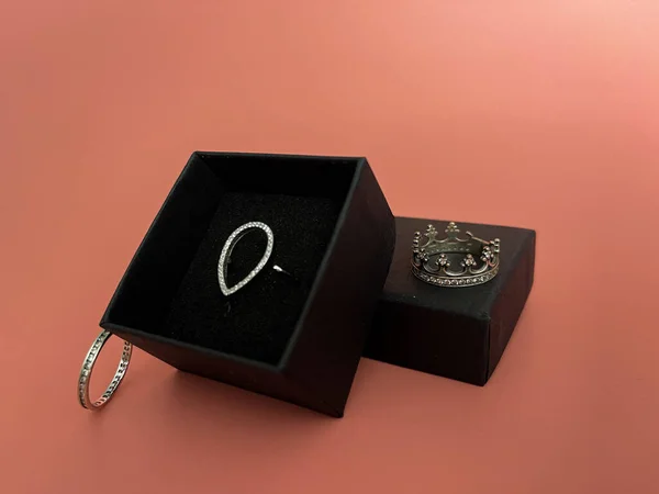 Kara bir kutuda, hassas bir arkaplanda Pandora tarzında bir düşüş şeklinde halka.