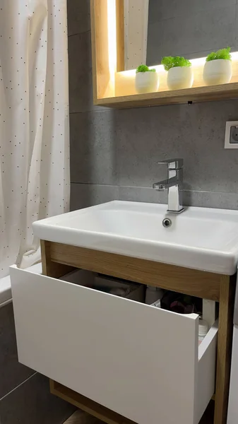 White sink on wood counter with a square mirror hanging above it. Bathroom interior.