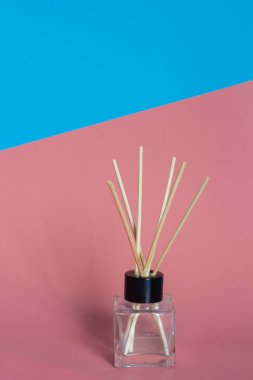 Home perfume bottle with perfume soaked incense sticks stands on blue and pink