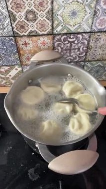 Kaynar suda khinkali pişirmek. Aşçı tavada kaşıkla hamur köftelerini karıştırıyor. yakın plan