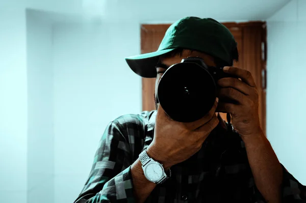 Genç adam odanın içinde DSLR kamerasıyla fotoğraf çekiyor. Adam içeride profesyonel bir kamerayla fotoğraf çekiyor. Elinde dijital kamera olan bir adamın yakınına..