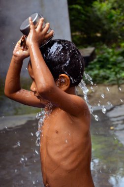 Closeup of a child taking bath with a mug. A kid pouring water with a jug and splashing water over head.