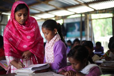 Gowainghat, Bangladeş - Kasım 06, 2019: Sınıftaki topluluk öğretmeni not defterini ve öğrencilerin matematik ödevlerini kontrol etmekle meşgul. Öğretmen hata buluyor ve öğrenciye nasıl yapılacağını öğretiyor..