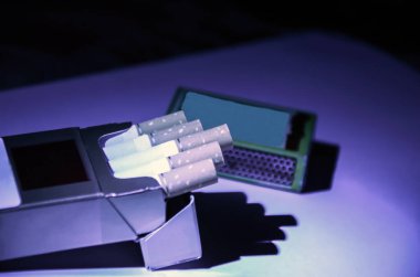 Bir paket sigara, paketten çıkan sigaralar ve sigara paketinin arkasında bir kibrit kutusu..