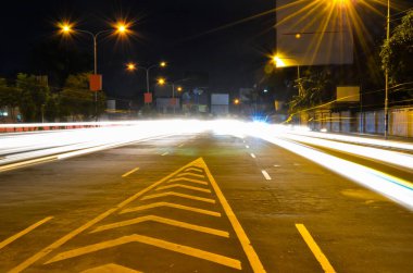 Gece ve araba otobanında yol ayrımcısının yakın çekimleri, uzun pozlu trafik ışıkları gökyüzünde bulanık trafik ışıklarıyla şeridi ayırıyor..