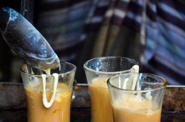 Çaya süt karıştırıyorum. Çay standında üç fincan sütlü çay hazırla. Köy çay yapma süreci. Çay tezgahı satıcısı çaya süt dökerek insanlara çay yapıyor..