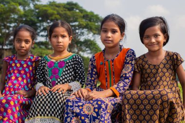 Gowainghat, Bangladeş - 06 Kasım 2019: Kızlar yerde oturuyor ve kameraya bakıyor. Kırsal kesimden fakir kızlar tatillerinin tadını çıkarıyorlar..