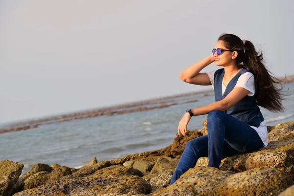 Beautiful young lady enjoying the sea beach wearing sunglass. Young girl wearing jeans and tops with a big smile on her face looking at the sea