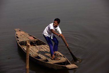 Taherpur, Bangladeş - 05 Kasım 2019: Okula gitmek için sandalın direksiyonunu tutan öğrenciye odaklanın. Küçük çocuk kürek çekiyor ve nehirde tahta kayık sürüyor.
