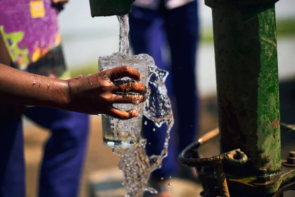 Children having fresh water from the tube well in a rural village to hydrate their bodies in the hot summer. Hand holding glass and splash of clean water from the tube well.