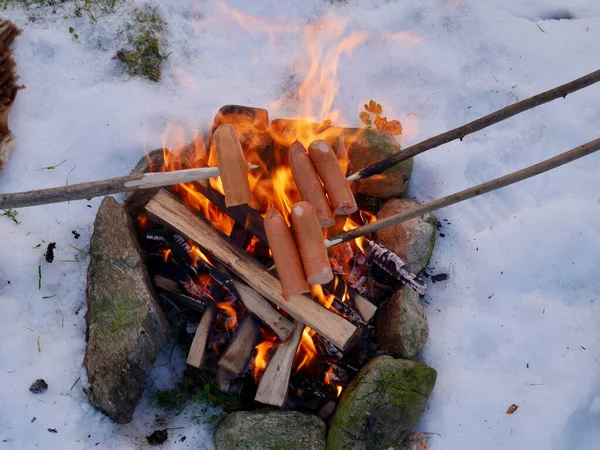 Leckere Würstchen am Stock über dem winterlichen Lagerfeuer braten. Konzept von Outdoor-Abenteuer und saisonalem Urlaub. — Stockfoto