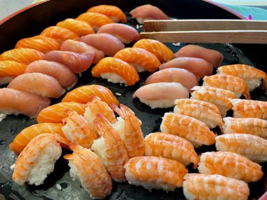 Taze suşi, karides, ton balığı, tereyağlı balık, somon, ahşap maşayla servis edilen siyah tablet. Yakın çekim..