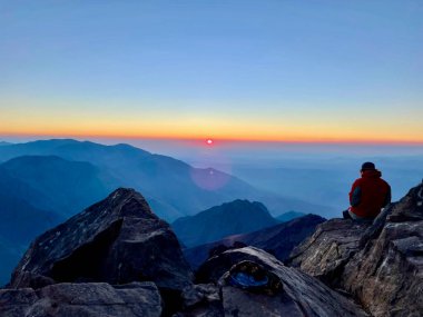 Yürüyüşçü, Kuzey Afrika 'nın en yüksek dağı Djebel Toubkal' ın tepesinde nefes kesen gün doğumunu izliyor. Fas.