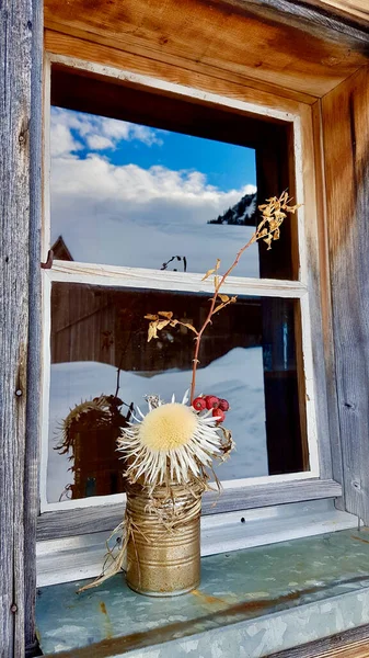 Gyönyörűen díszített ablak egy fából készült hegyi kunyhóban tükröződik a téli táj benne. Frastanz, Vorarlberg, Ausztria. — Stock Fotó