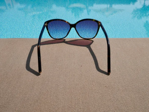 Primer plano de gafas de sol colocadas junto a la piscina. Fondo horario de verano, vacaciones, concepto de viaje. — Foto de Stock
