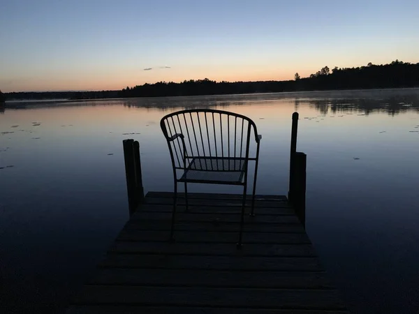 Silhouette of a chair on a deck of Ox Lake at sunrise. Minnesota, USA. — Fotografia de Stock