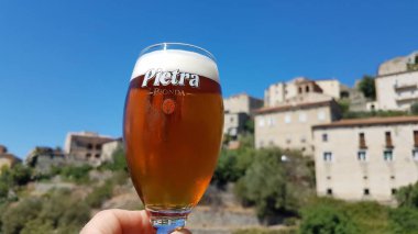 Lama, Korsika, 8.08.2020. Bir bardak taze çekilmiş Pietra, Korsika kestane birası, Lama 'ya karşı, dağlarda kurulmuş rüya gibi bir tepe kasabası..