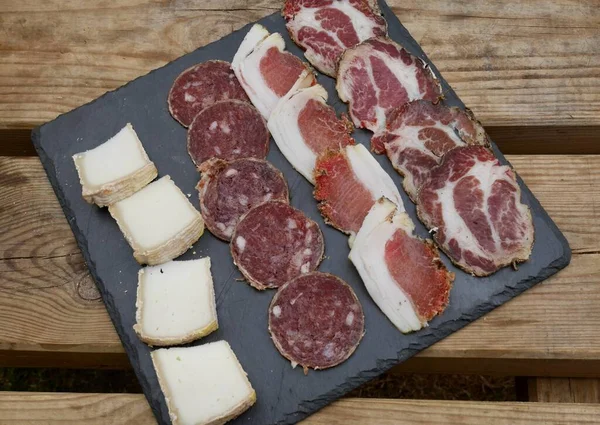Corsican specialities, Coppa, Lonzo, salami sausage and goat cheese served on black stone plate. — Fotografia de Stock