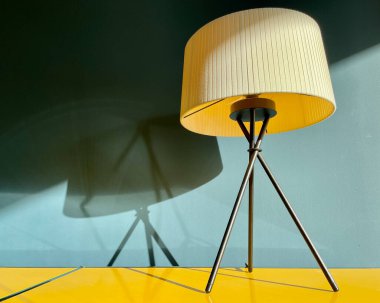 Mavi duvarın önündeki sarı bir büfede bir masa lambasının yakın çekimi..