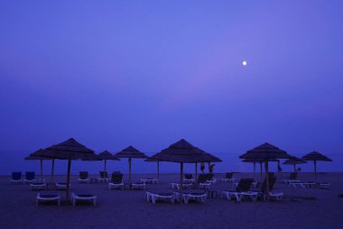 Dolunaylı bir gecede kumsalda şezlonglar ve saman şemsiyeler. Yüksek kalite fotoğraf