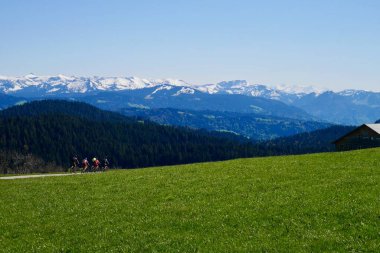 Pfaender yakınlarındaki Hochberg ovasında bisikletçiler, arka planda karlı dağlar. Vorarlberg, Avusturya.