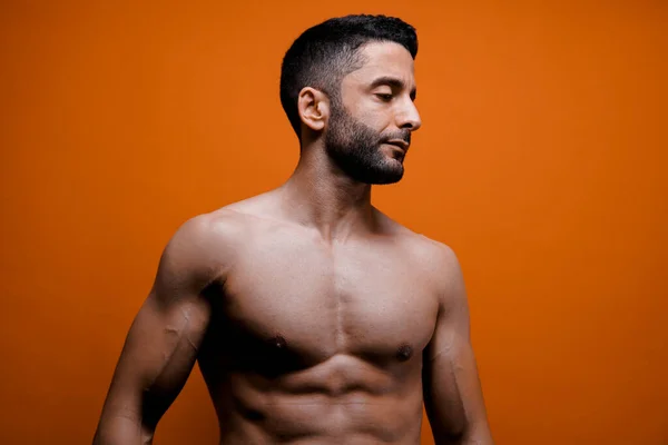 Turuncu arka planda kaslı vücudu olan kendinden emin bir erkek. Yakışıklı, seksi erkekler. Erkek güzeli reklam arkaplanı. Karın kasları ve karın kasları olan zinde adam..
