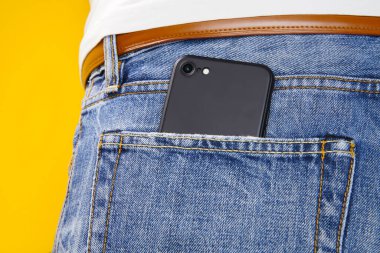 Sarı arka planda kot pantolon cebinde cep telefonu. Sosyal medya kavramı ve her zaman online.