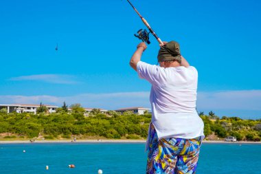 Kadın Fisher yazın sahilde balık yakalıyor. Balıkçı kadın yazın balık tutuyor. Elinde olta olan kadın. Yaşlılar için mutlu ve renkli hobi kavramı.