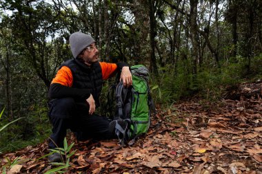 Kolombiya 'nın kuru yaprakları ve yanında yeşil bir sırt çantasıyla ormanda maceraya atılan bir adam.