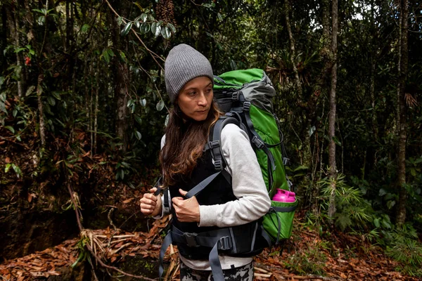 Kolombiya 'nın kuru yaprakları ve yanında yeşil bir sırt çantasıyla ormanda maceraya atılan bir kadın.