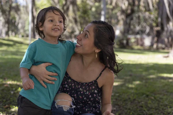 Amerikalı Latin anne, 3 yaşındaki oğluyla parkta mutlu bir şekilde sarılıyor. Aile ve anneler günü konsepti.