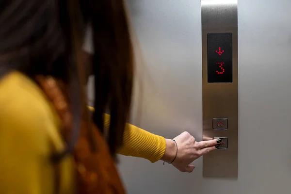 Alışveriş merkezindeki tanınmayan genç Latin Amerikalı kadın (23) asansör düğmesine basıyor. Sarı uzun kollu flanel giyiyor. Taşınma kavramı