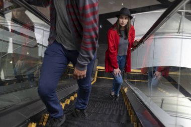 Genç Latin Amerikalı kadın (23) bir alışveriş merkezinde yürüyen merdivende yürüyor. O, siyah bir şapka ve kırmızı bir kazak giyiyor. Yürüyüş ve eğlence konsepti.