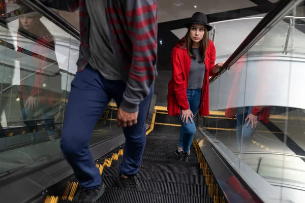 Genç Latin Amerikalı kadın (23) bir alışveriş merkezinde yürüyen merdivende yürüyor. O, siyah bir şapka ve kırmızı bir kazak giyiyor. Yürüyüş ve eğlence konsepti.