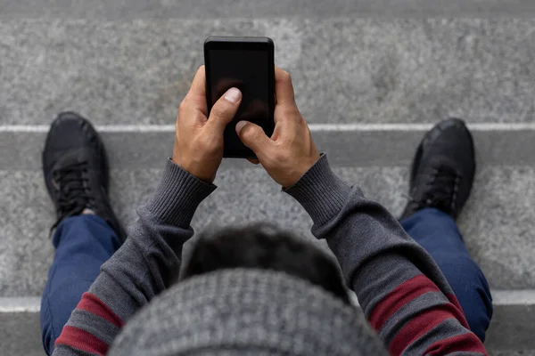 Genç erkek (22) tanınmayan Latin Amerikalı merdivenlerde cep telefonunu kontrol ediyor. Yukarıdan bak. Teknoloji konsepti.