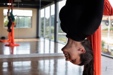 Sınıfta gülümseyen Latin Amerikalı kadın havadan jimnastik kumaşlarıyla ters poz veriyor. Yoga ve sağlık konsepti.