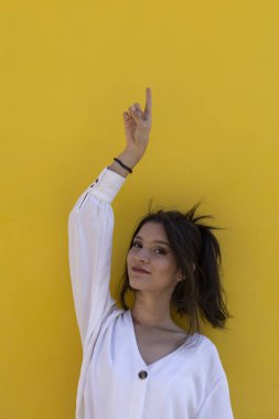 Gülümseyen genç Latin Amerikalı kadın portresi (24) sarı arka planda tek parmağıyla boş üst boşluğa izole edilmiş. Tanıtım indirimi teklifini kabul et.