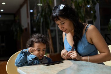 Anne ve Latin Amerikalı oğlu cep telefonundan video izlerken eğleniyorlar. Annelik ve Anneler Günü konsepti.