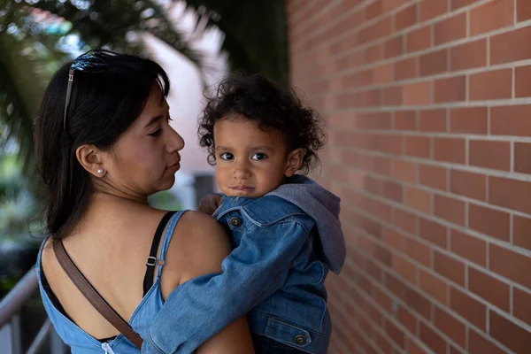 Latin Amerikalı anne yürürken çocuğunu kollarında taşıyor. Yürüyüşe çık annelik.