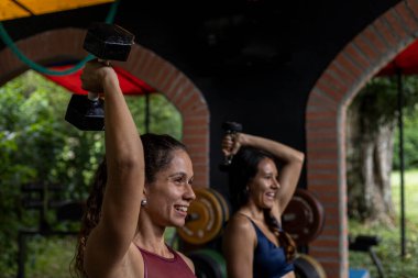 İki Latin Amerikalı kadın, spor salonunda dambıl kullanarak yüksek yoğunluklu egzersiz yapıyorlar. Sağlıklı Yaşam Tarzı Konsepti