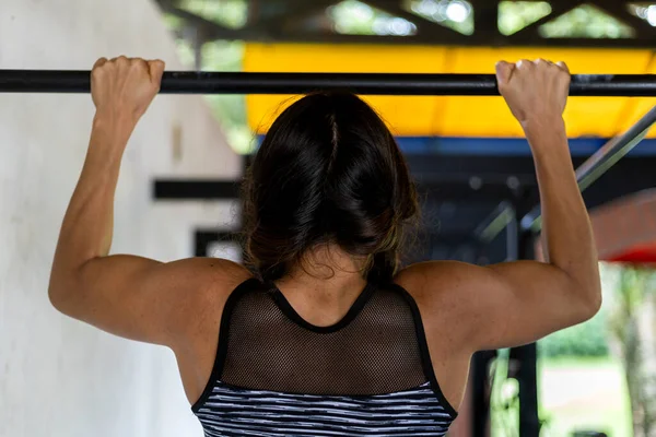 Genç Latin Amerikalı kadın spor salonundaki egzersiz sırasında kolunun gücünü jimnastik barda test ediyor. Tanınmaz halde. Sağlıklı Yaşam Tarzı Konsepti.