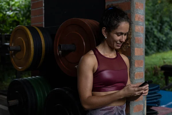 Smiling Latin American Woman Uses Her Cell Phone Gym Concept — Stockfoto