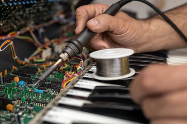 Latin Amerikalı elektronik teknisyeninin elleri servis merkezinde lehim ve teneke lehim kullanarak piyanonun devresini tamir ediyor. Konsept onarımı, müzik, elektronik