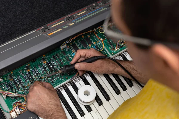 Latin American electronic technician fixes a piano with soldering iron and tin at the service center. Concept repair, Music, electronic