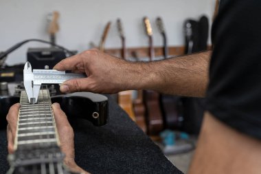Latin Amerikalı Luthier bir elektro gitarın tellerini bir vernier ile doğru olarak kalibre eder. Tanımlanamayan kişi. Gitar konsepti, kalibrasyon, alet.