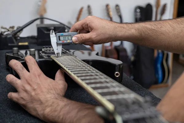 Latin Amerikalı Luthier elektro gitarın tellerini dijital bir vernier ile kalibre ediyor. Tanınmaz halde. Gitar konsepti, kalibrasyon, alet.